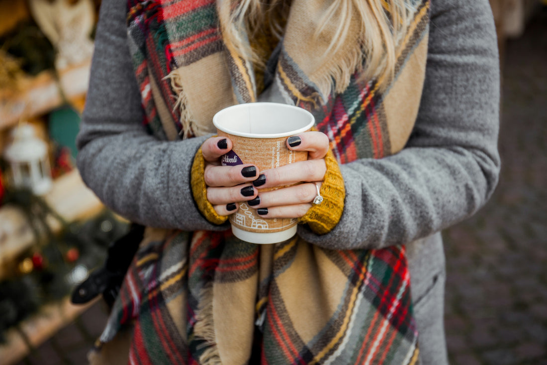 Woman holds a warm drink at a holiday market.